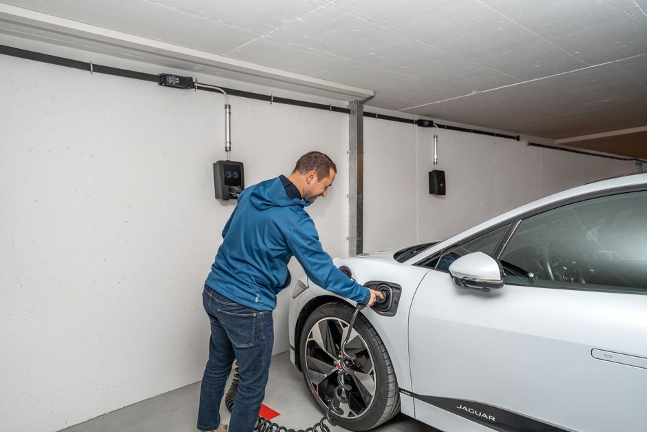 A man plugging a white electric car into a wall-mounted charger in a home garage