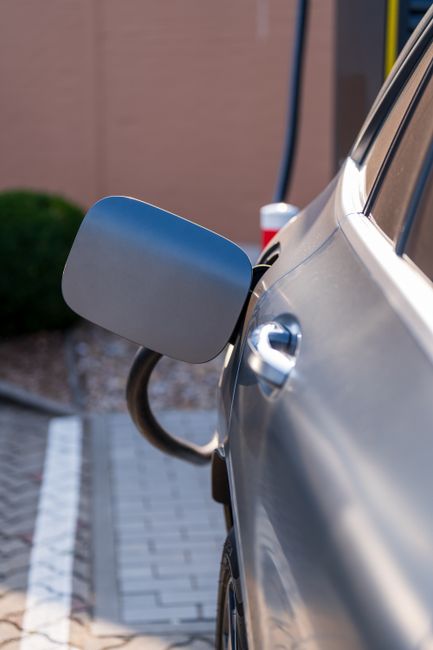 A silver electric car with its charging flap open and a cable plugged in at a charging bay